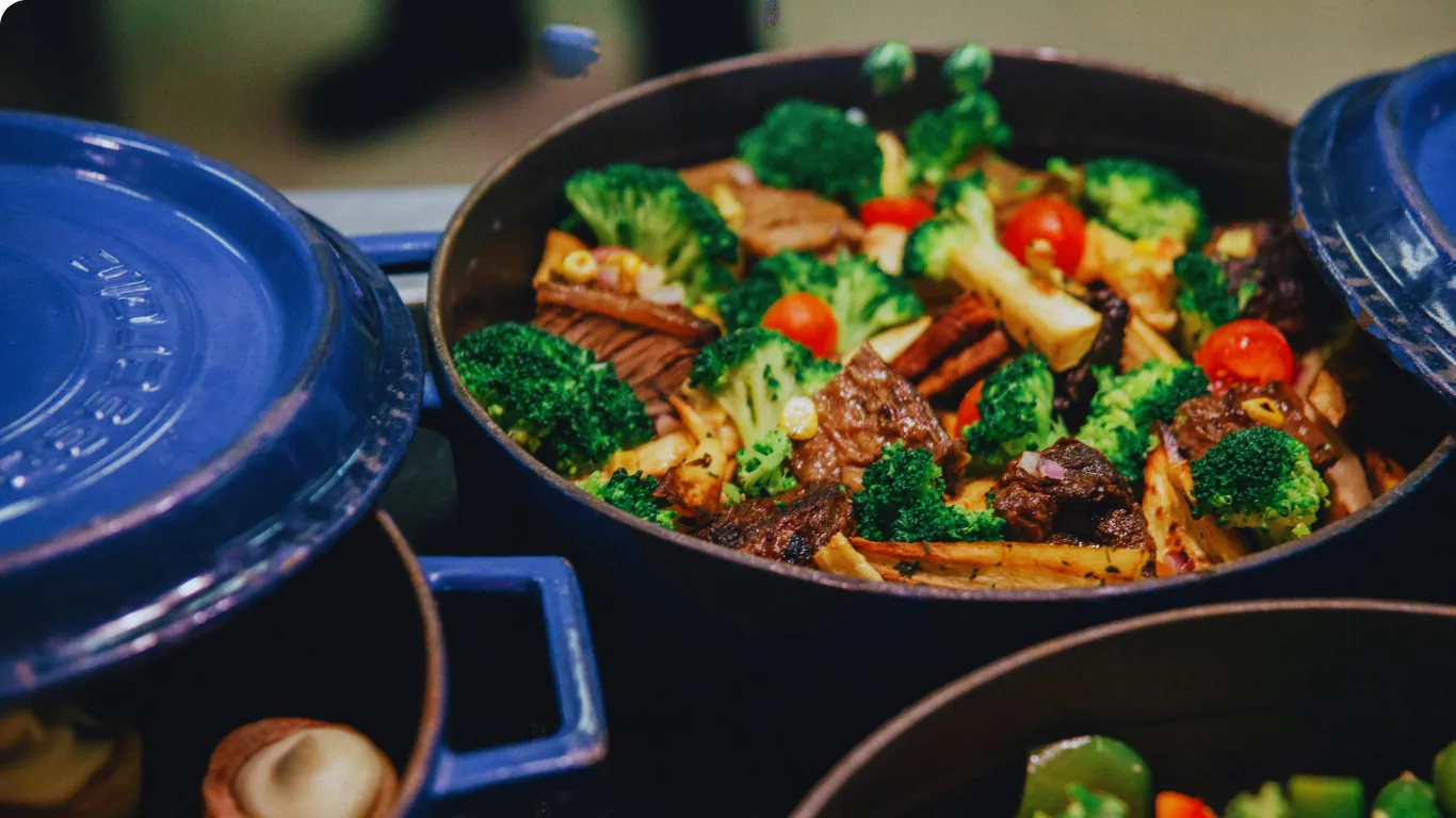 A cast-iron pot of braised beef with broccoli and tomatoes, ready to portion